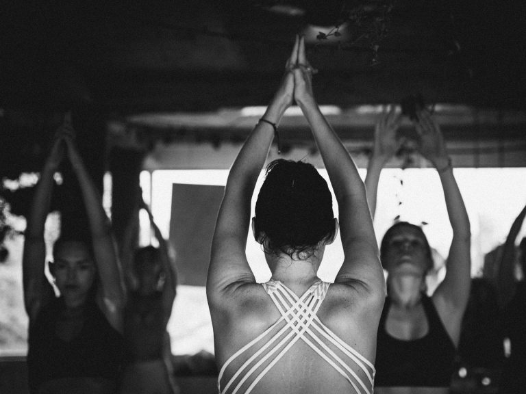 Gruppe von Frauen in Yoga-Pose, Hände über dem Kopf, fokussierte Atmosphäre.
