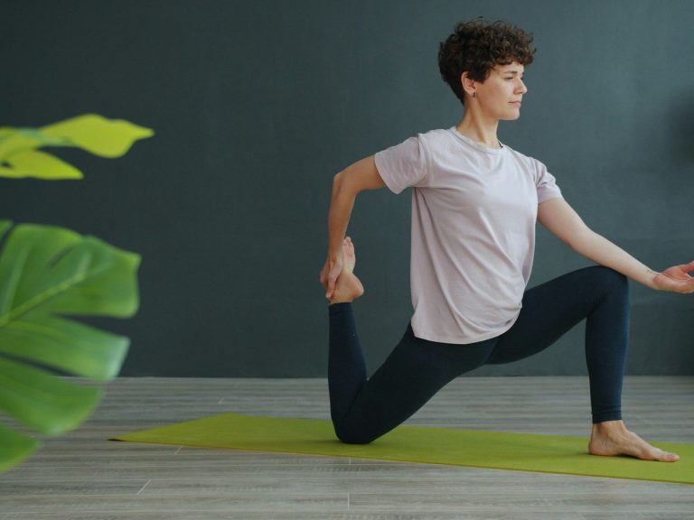 Junge Frau in Yoga-Pose auf einer Matte vor einer neutralen Wand.