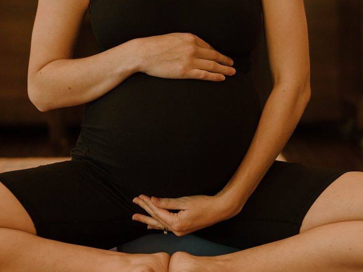 Schwangere Frau sitzt im Meditationspose und hält ihren Bauch.