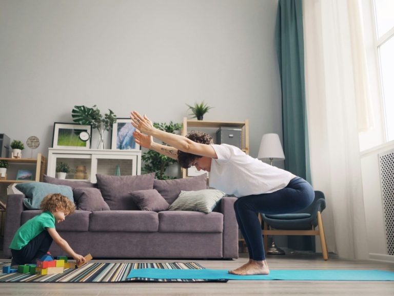 Mutter macht Yoga neben einem spielenden Kind im Wohnzimmer.