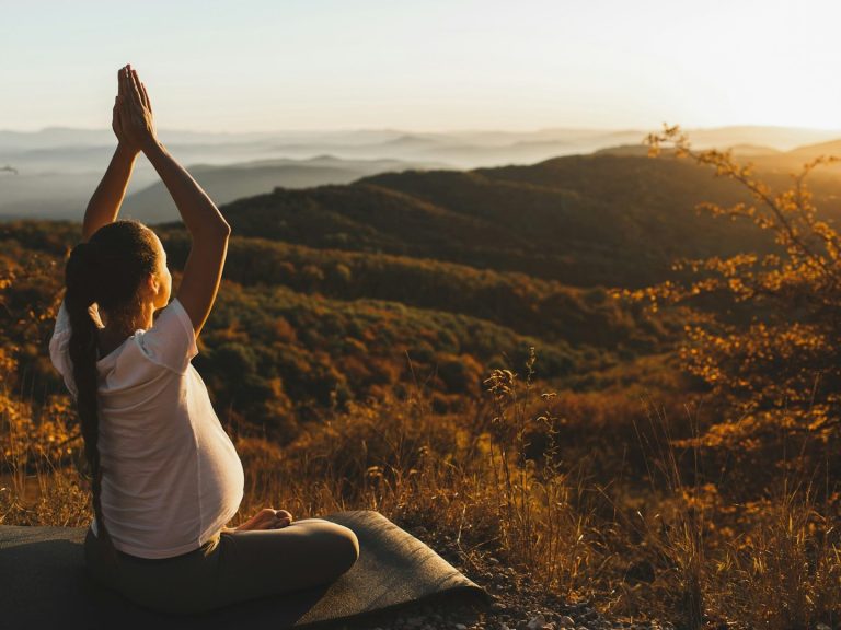 Schwangere meditiert im Schneidersitz vor einer malerischen Berghorizont bei Sonnenaufgang. Macht Yoga
