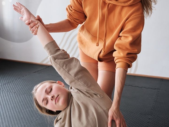 Eine Person hilft einer anderen, eine Yoga-Position zu halten, beide in Sportkleidung.
