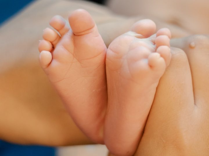 Kleinkindfüße, die sanft von einer Hand gehalten werden.