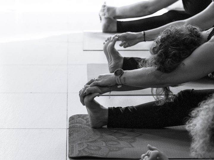 Personen dehnen ihre Beine und Arme auf Yogamatten in einem hellen Raum.